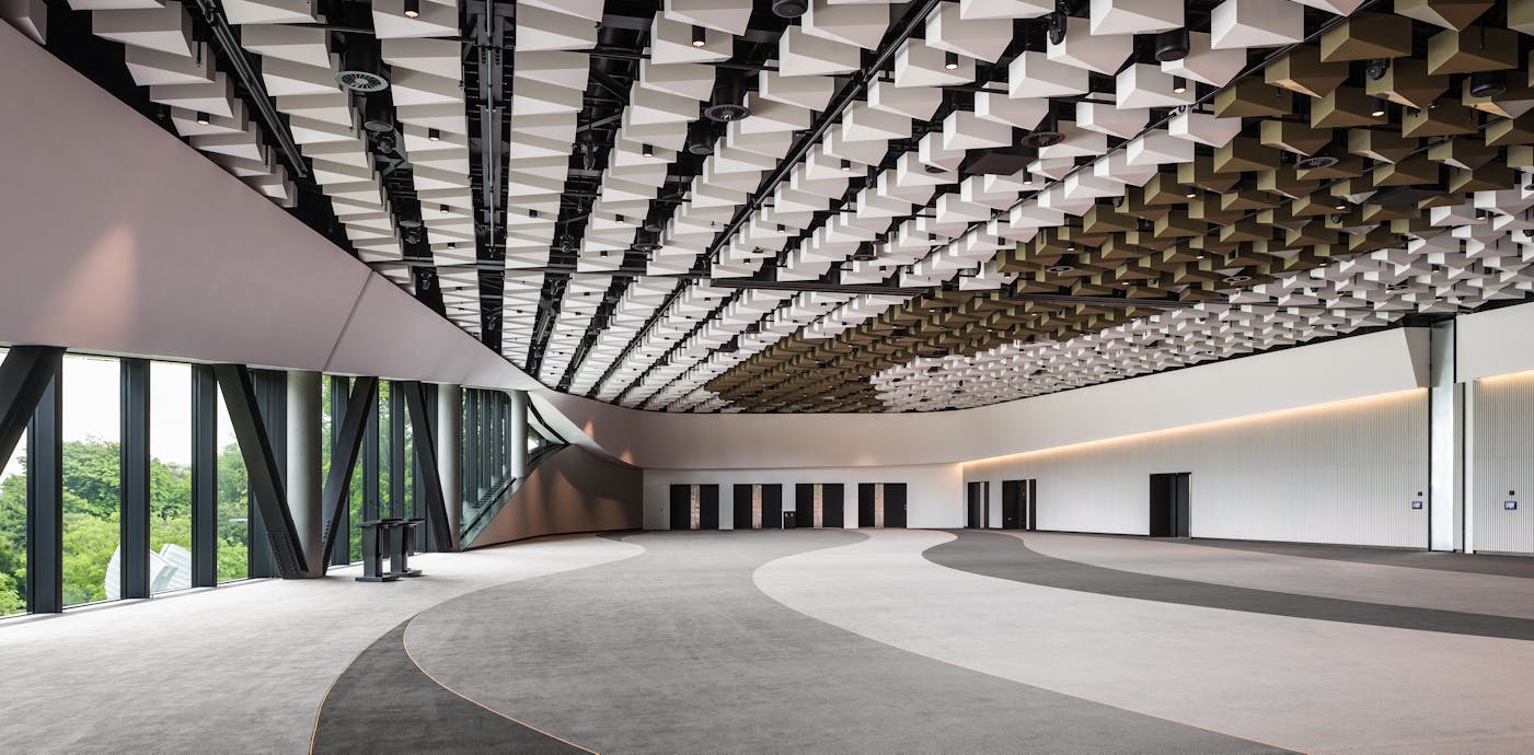 A spacious, modern conference room featuring a dynamic ceiling design, curved carpet patterns, and large windows overlooking greenery.